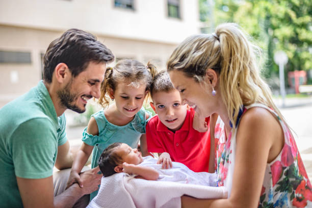 Happy parents with three kids. There is newborn baby, a boy and a girl. All of them are watching newborn baby. Happy family!