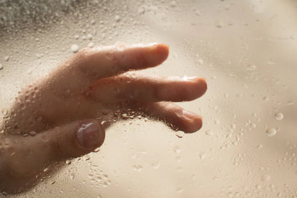 istock young womans hand behind a glass with water drops 1185414759