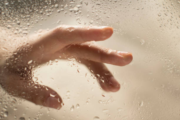 istock young womans hand behind a glass with water drops 1185414760
