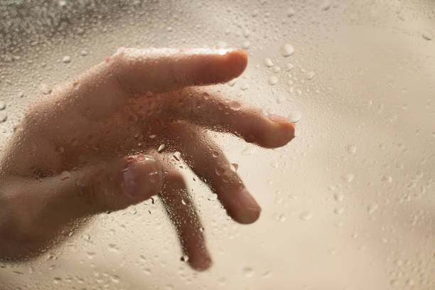 istock young womans hand behind a glass with water drops 1185414763