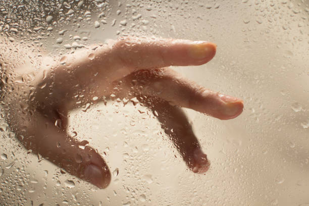 istock young womans hand behind a glass with water drops 1185414775