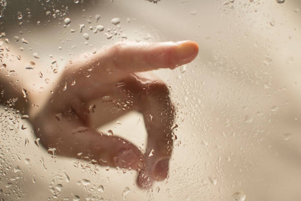 istock young womans hand behind a glass with water drops 1185414778