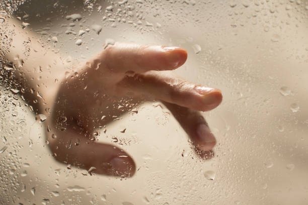 istock young womans hand behind a glass with water drops 1185414779