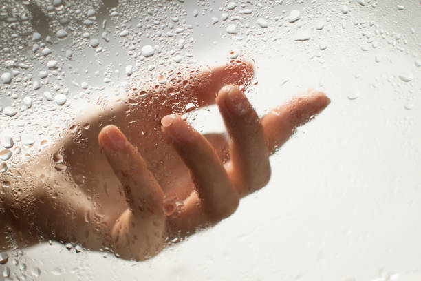 istock young womans hand behind a glass with water drops 1185414789