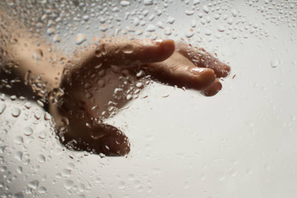 istock young womans hand behind a glass with water drops 1185414798