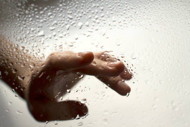 istock young womans hand behind a glass with water drops 1185414804
