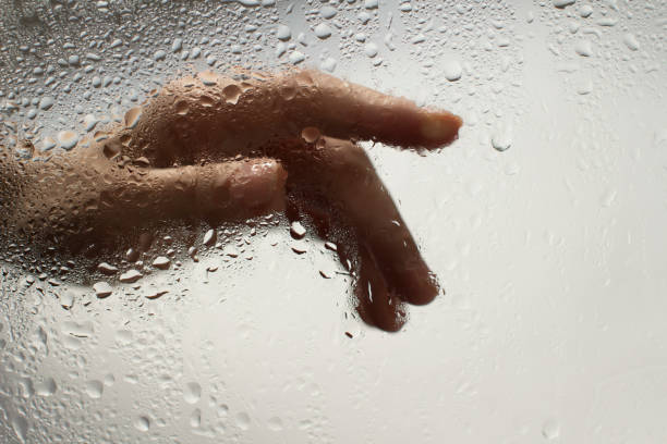 istock young womans hand behind a glass with water drops 1185414819