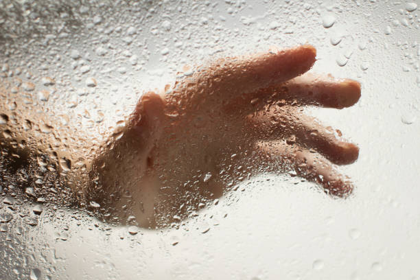 istock young womans hand behind a glass with water drops 1185414836