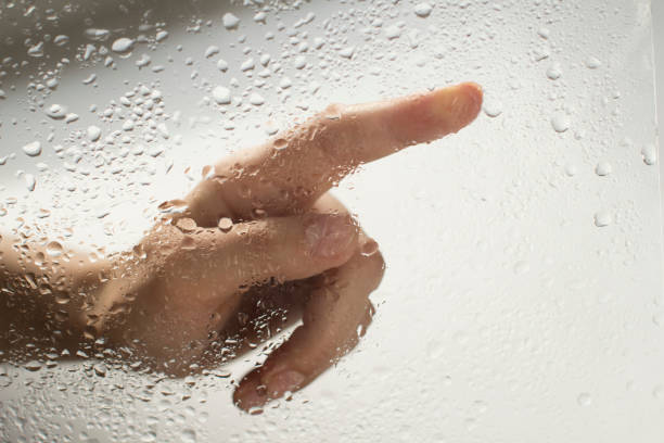 istock young womans hand behind a glass with water drops 1185414847
