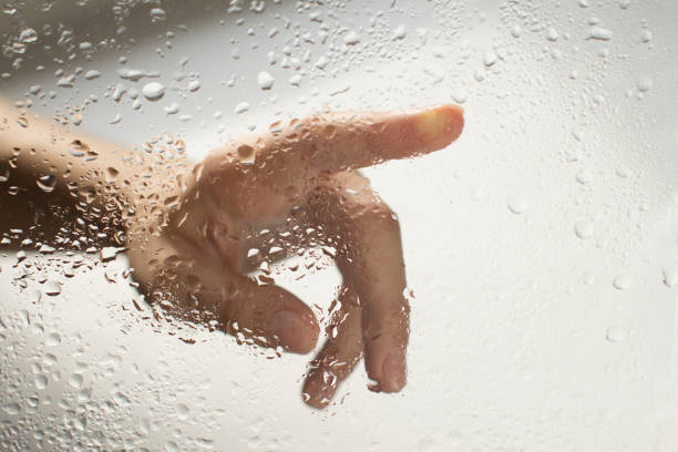 istock young womans hand behind a glass with water drops 1185414848