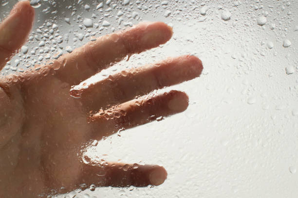 istock young womans hand behind a glass with water drops 1185414853