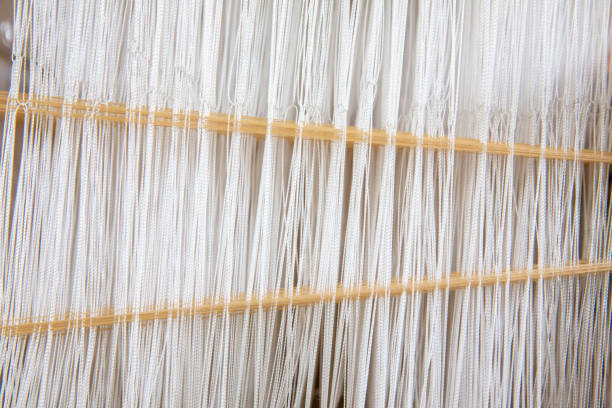 istock Close-up weaving cotton on manual loom. Selective focus of cotton thread on weaver machine. Thai cotton handmade. Homespun fabric process. The process of fabric weaving in vintage weaver machine. 1185415064