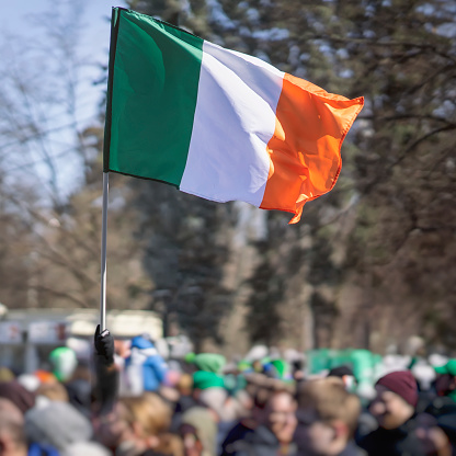 National Flag of Ireland close-up in hand on background of crowd people during the celebration of St. Patrick's Day in park, traditional carnival
