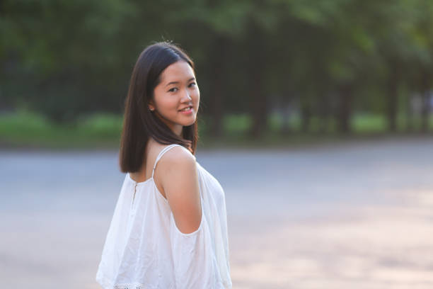 female nature keeps his hat summer sun sunset looks pleased. azitka woman black hair white shirt black shorts out trees around.