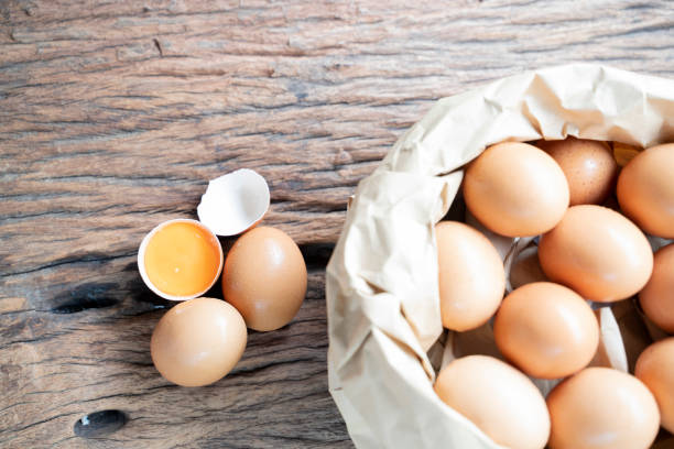 istock Broken eggs containing and egg yolks on table wooden floors and eggs in brown bag. 1185429328