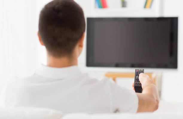 istock man watching tv and changing channels at home 1185430623