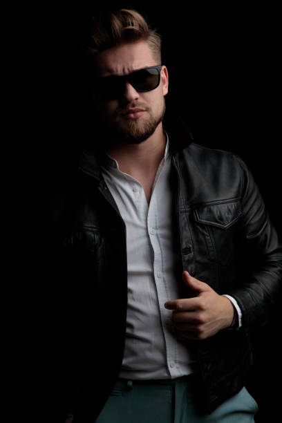 istock casual man wearing sunglasses standing and fixing his leather jacket 1185431557