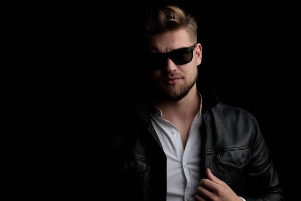 istock casual man wearing sunglasses standing and arranging jacket 1185431579