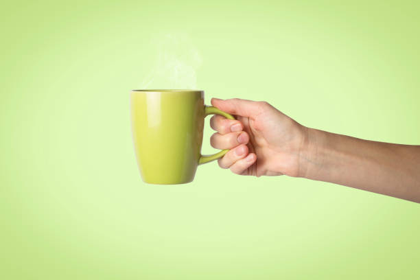 istock Female hand holding a green cup on a green background. Side view 1185435316