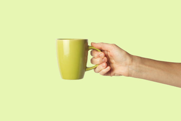 istock Female hand holding a green cup on a green background. Side view 1185435422