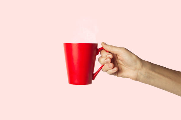 istock Female hand holding a red cup with hot coffee on a pink background. Side view 1185435773