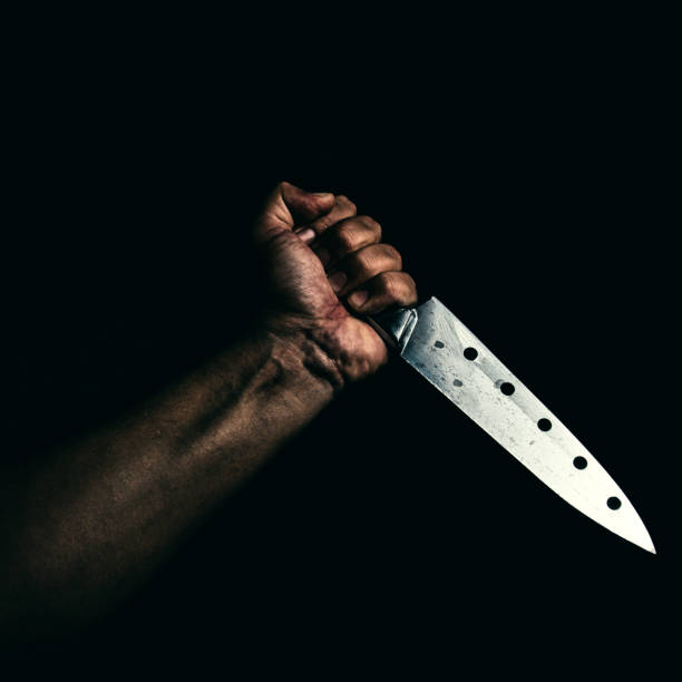istock Man with bloody knife, hand close up, dark background 1185438321