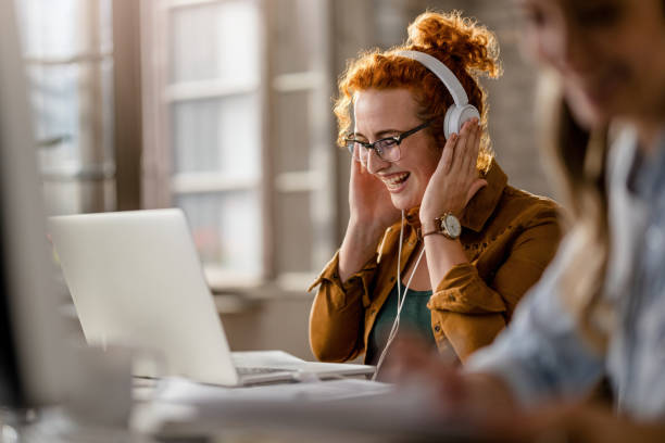 istock Happy creative woman wearing headphones while using laptop in the office. 1185442378