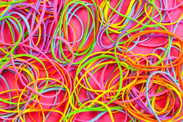 Close up of a pile of neon colored elastic rubber bands of red, orange, yellow, green and blue against a pink background