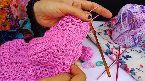 woman crocheting a pink girl dress with wool and hook.close up shot of professional crocheting woman.