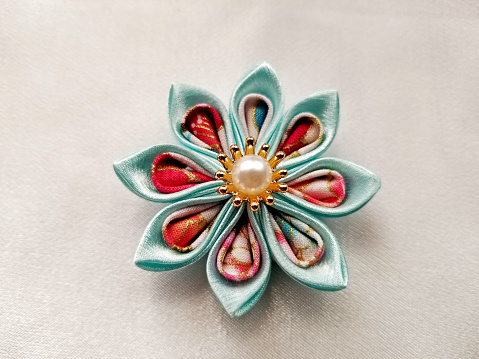 Japanese kanzashi hand made flower constructed from kimono material and displayed on an ivory background