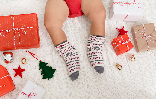 Christmas holidays. Little baby legs in winter socks with Xmas gifts, top view