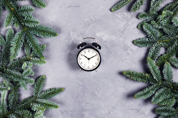 istock Black clock on grey concrete background with Christmas branches. 1185448980