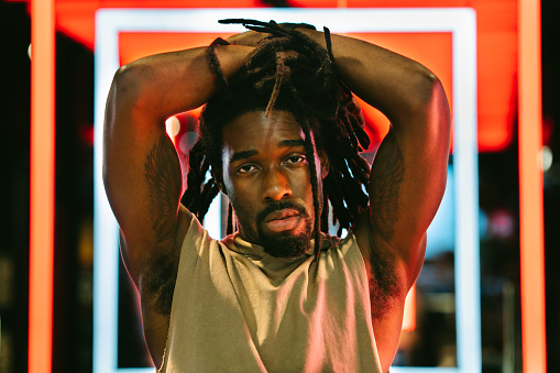 A portrait of a handsome black man in front of colorful neon lights.