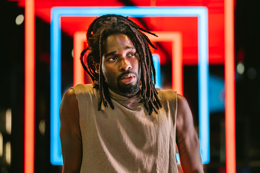 A portrait of a handsome black man in front of colorful neon lights.