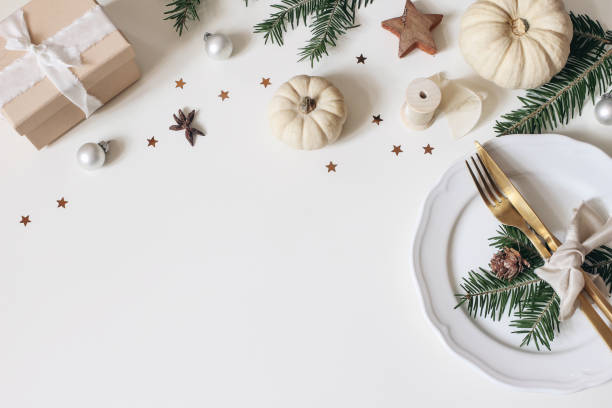 Traditional Christmas table place setting. Golden cutlery, porcelain plate, fir tree branches, gift box, pine cones and white pumkins. Christmas baubles decoration. Holidays background. Flat lay, top. stock photo