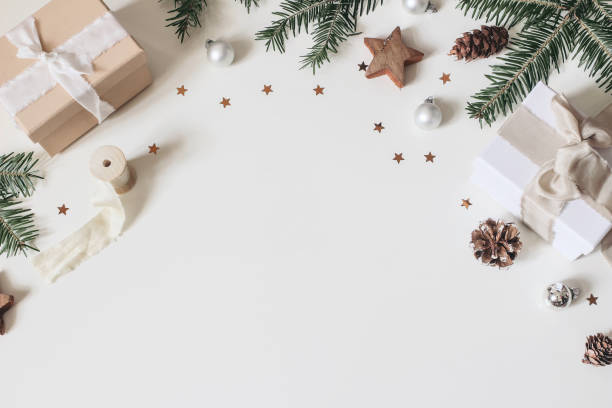 Winter festive frame composition. Pine cones, silk ribbons, fir tree branches, gift wrapped boxes, Christmas balls, baubles and stars confetti isolated on white table background. Flat lay, top view.