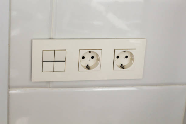 istock Two white socket and switch on the wall with tiles in the hotel bathroom with white tiles  on the wall. Bathroom luxury interior 1185454579