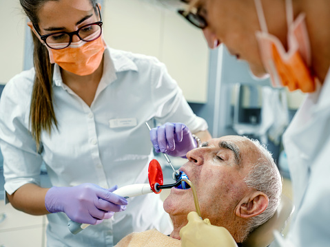 Female dentist treating patient senior man teeth.
