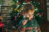 Little boy eating candy near Christmas tree at home