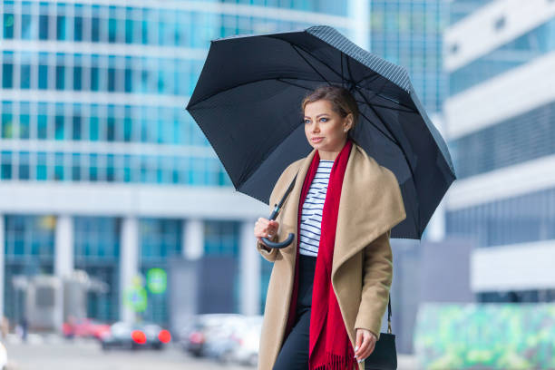 雨。見事なブルネットの女の子のアウトドアライフスタイルファッションの肖像画。街の通りを歩く。買い物に行く。スタイリッシュな白フィットコート、赤いネックスカーフ、黒い傘のス� - neckscarf ストックフォトと画像