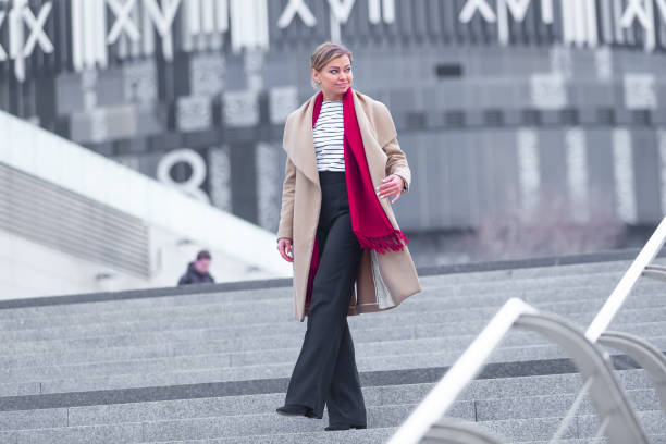 at the mall lifestyle fashion portrait of stunning brunette girl. walking on at the mall. going shopping. wearing stylish white fitted coat, red neckscarf. business woman. black bag - neckscarf imagens e fotografias de stock