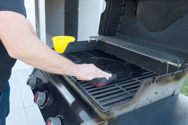 The male hand cleans the black grill with a soft brush. Grill for frying meat. Cleaning the outdoor gas grill in the backyard. The male hand cleans the black grill with a soft brush. Grill for frying meat. Cleaning the outdoor gas grill in the backyard. metal grate photos stock pictures, royalty-free photos & images