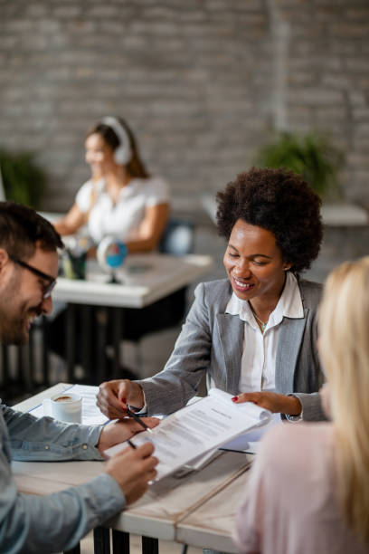 happy african american insurance agent showing to a couple where to sign the contract. - women men signing business imagens e fotografias de stock