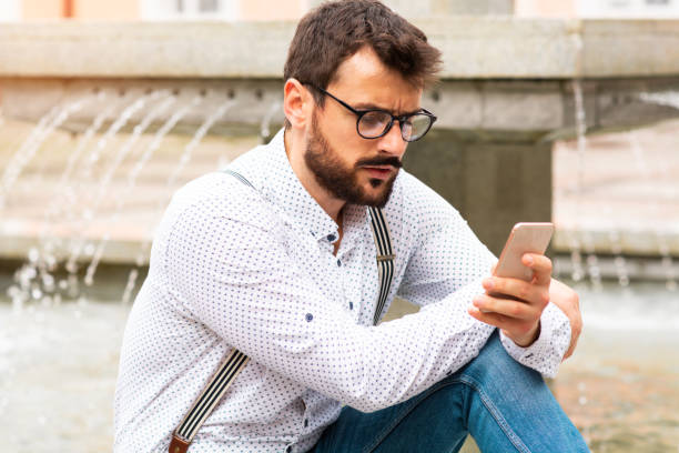 istock Man sitting on fountaing and using smart phone. 1185467075
