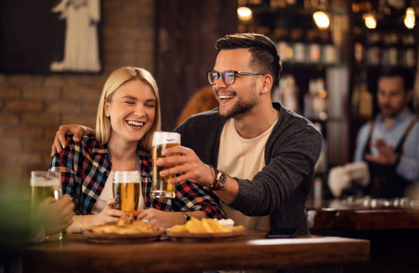 Cheerful couple toasting with beer and having fun in a pub. Young happy couple having fun together while toasting with beer in a bar, couple drinking stock pictures, royalty-free photos & images