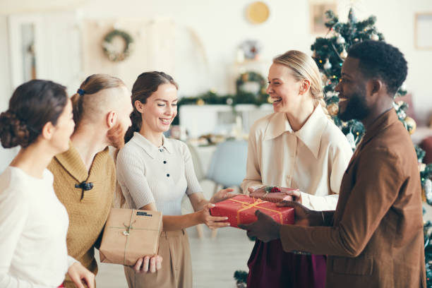 Enjoying Christmas Presents Waist up portrait of cheerful young people exchanging presents during Christmas party in cozy interior, copy space office christmas party stock pictures, royalty-free photos & images