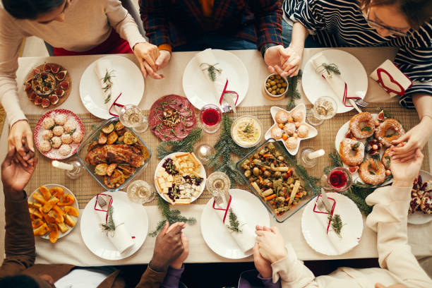 Saying Grace at Dinner Above View Above view at group of people sitting at dining table on Christmas and joining hands in prayer, copy space winter food top view stock pictures, royalty-free photos & images