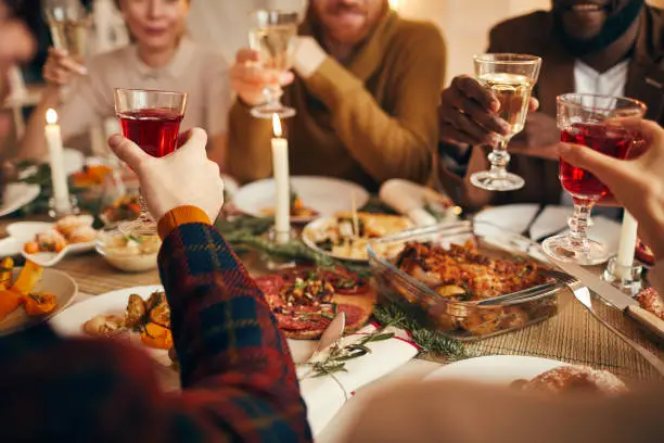 Close up of modern adult people raising glasses while enjoying Christmas dinner at home, copy space