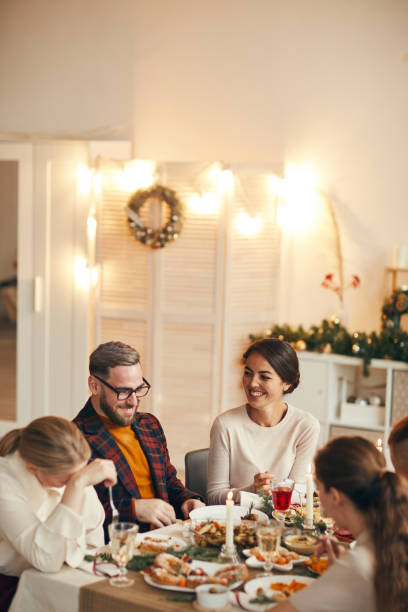 People Enjoying Dinner on Christmas High angle view at successful adult couple laughing cheerfully while celebrating Christmas with friends at dinner table, copy space family christmas party stock pictures, royalty-free photos & images