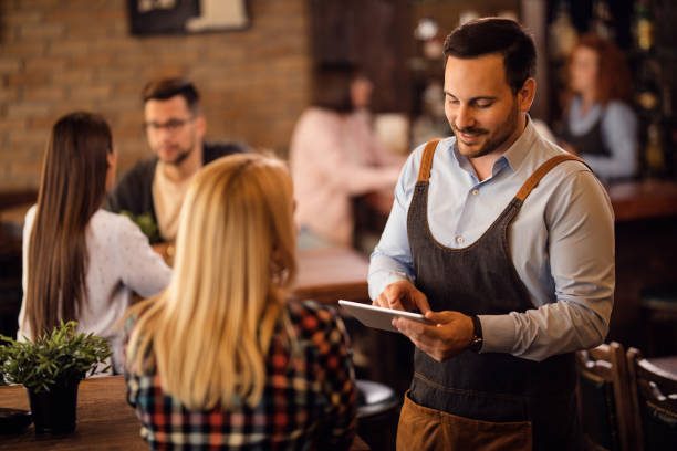 istock Happy waiter writing an order on touchpad while serving a guest in a pub. 1185468545